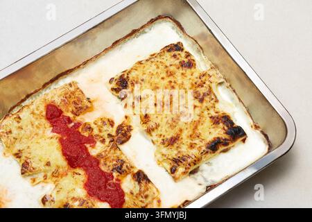 Vue aérienne de cannellonis italiens cuits au four recouverts de fromage fondu et de sauce tomate, servis dans un plat de cuisson en métal avec une béchamel crémeuse pour un moment de confort Banque D'Images
