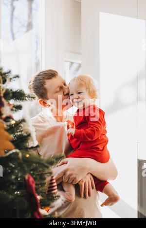 Père embrassant son fils bébé souriant près du sapin de Noël Banque D'Images