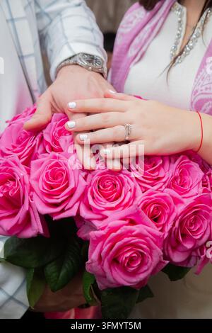 Close up de mains de couple montrant une bague de fiançailles sur un bouquet luxuriant de roses rosesMoment romantique capturant l'amour et la demande en mariage avec Banque D'Images