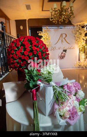 Décorations florales luxueuses placées sur une table devant une toile de fond personnalisée pour un événement. Magnifiques bouquets de fleurs et un immense arrangement de roses rouges Banque D'Images