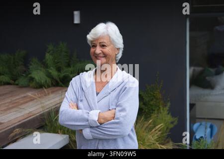 Sénior portant un sweat à capuche gris clair, debout les bras croisés sur la terrasse près du plancher Banque D'Images