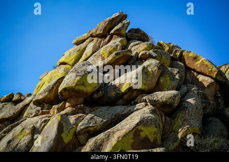 Un énorme tas de gros blocs de granit arrondis, dont beaucoup sont recouverts de taches de lichen jaune-vert vif, s'élève sous un ciel bleu éclatant. Le rugueux-t Banque D'Images
