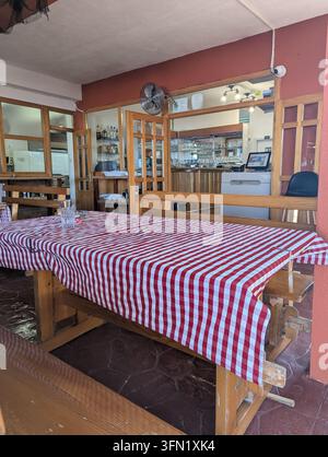 Pirovac, Croatie, 16 août 2026 Intérieur de restaurant calme avec des tables en bois, des nappes à carreaux rouges, de la verrerie, des étagères de bar, un passe-plat et ce Banque D'Images