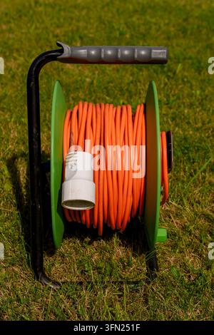 Bobine de câble d'extension orange sur l'herbe verte dans le jardin Banque D'Images
