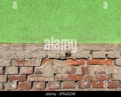 Un vieux mur de briques rouges partiellement recouvert d'un plâtre vert texturé, créant un contraste frappant entre la maçonnerie apparente et la surface usée. La a Banque D'Images