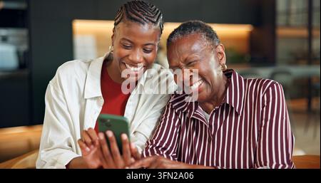 Mère âgée, riant et femme avec téléphone à la maison, divertissement ou visionnage de vidéo avec fille. Famille, en ligne et lien avec parent âgé Banque D'Images