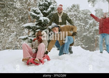 Groupe divers d'amis faisant de la luge et s'amusant dans un parc d'hiver Banque D'Images