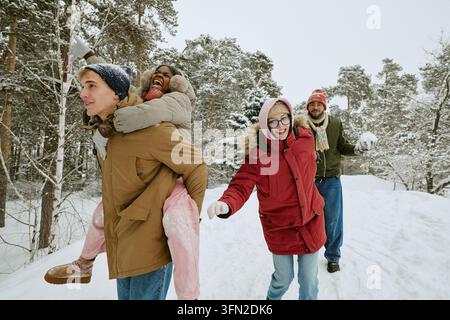 Groupe divers d'amis jouant et s'amusant dans une forêt enneigée en hiver Banque D'Images