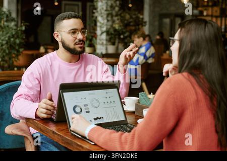 Divers collègues discutant un projet commercial sur des ordinateurs portables dans un café Banque D'Images