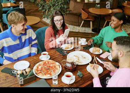 Groupe divers d'amis mangeant une pizza avec un smartphone dans un café Banque D'Images
