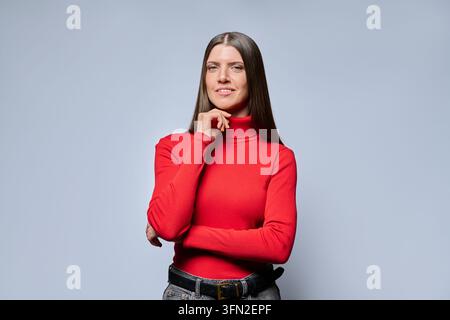 Jeune femme pensive avec la main sur le menton devant un fond gris de studio Banque D'Images