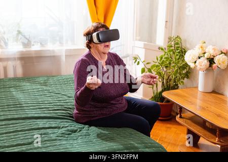 Ancienne dame assise confortablement sur un canapé, portant des lunettes de réalité virtuelle et profitant d'expériences immersives. La technologie transforme les loisirs pour la moderne Banque D'Images