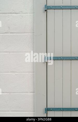 Volet en bois gris minimaliste avec charnières métalliques, mur de briques peint en blanc, arrière-plan de détails architecturaux épurés Banque D'Images