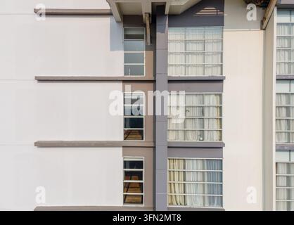 Vue aérienne d'une façade de bâtiment moderne présentant des murs blancs et gris immaculés, de grandes fenêtres avec des rideaux blancs et des lignes architecturales horizontales en Banque D'Images