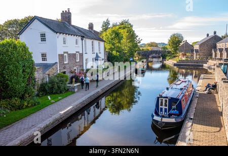 Des gens marchent le long d'un chemin pavé longeant une voie d'eau calme avec des bateaux de canal amarrés et des maisons blanches historiques sous un ciel d'après-midi lumineux Banque D'Images