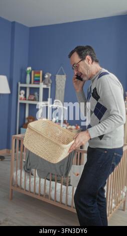 Homme au téléphone plaçant le lapin en peluche dans le panier à côté du berceau dans le bâtiment de la chambre de bébé ; organisation des soins. Banque D'Images