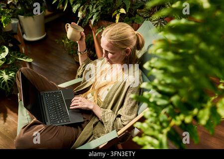 Freelance femme travaillant sur un ordinateur portable à domicile entourée de plantes Banque D'Images