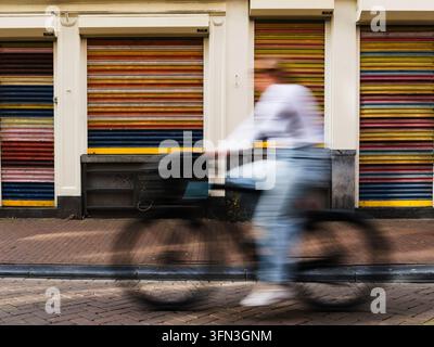 Un cycliste flou passe devant des volets roulants rayés colorés sur la Nieuwe Hoogstraat dans le centre d'Amsterdam, Pays-Bas Banque D'Images