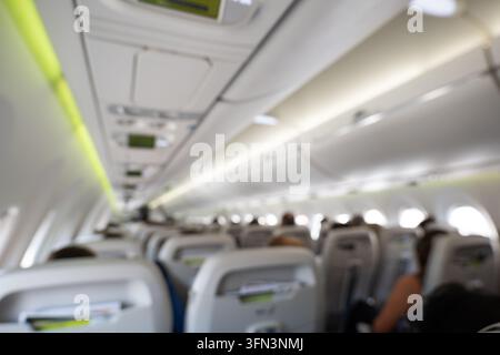 Perspective intérieure floue de la cabine d'un avion commercial montrant des sièges estompés et des compartiments à bagages au-dessus des sièges dans une lumière ambiante douce pendant Banque D'Images