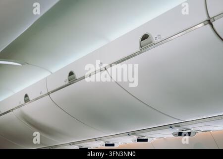 Vue en perspective le long des compartiments à bagages fermés et des numéros de rangée montés à l'intérieur de la cabine d'un avion de ligne moderne pendant Banque D'Images