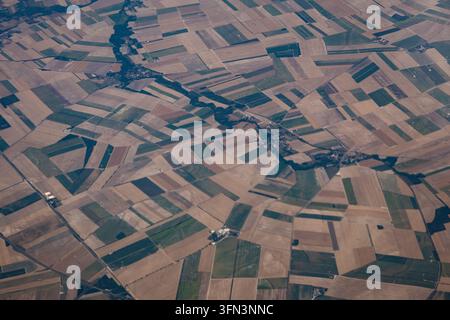 Photographie aérienne prise depuis une grande altitude, regardant directement vers le bas sur un mosaïque variée de champs agricoles géométriques, de petits villages et de lignes d'arbres Banque D'Images