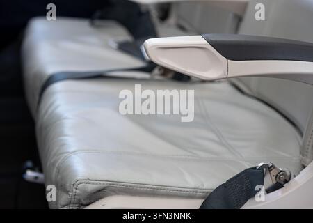 Vue détaillée montrant un siège passager en cuir gris vide, un accoudoir et une ceinture de sécurité à l'intérieur de la cabine d'un avion commercial pendant la préparation du vol Banque D'Images