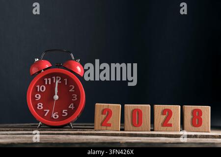Réveil rouge avec blocs de bois indiquant l'année 2028 sur fond sombre Banque D'Images