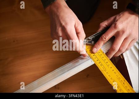 Homme marquant une mesure sur un profilé métallique avec un crayon et une règle, gros plan des mains pendant les travaux de préparation. Espace de travail intérieur, concept de mise en page précise et de planification de construction Banque D'Images
