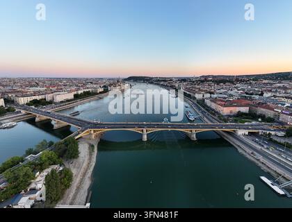 Vue aérienne du pont Marguerite sur le Danube, avec le Parlement hongrois, des bateaux fluviaux et le trafic nocturne le long des quais à Budapest, Hongrie Banque D'Images