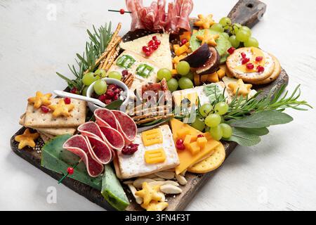 Planche de charcuterie élégante avec du fromage, des viandes séchées et des fruits pour une fête de Noël sur un fond clair. Vue de dessus. Banque D'Images