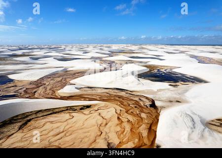 Une vue aérienne impressionnante par drone des motifs de sédiments complexes qui serpentent à travers une petite rivière entourée de dunes de sable blanc à Lencois Maranhenses. Banque D'Images