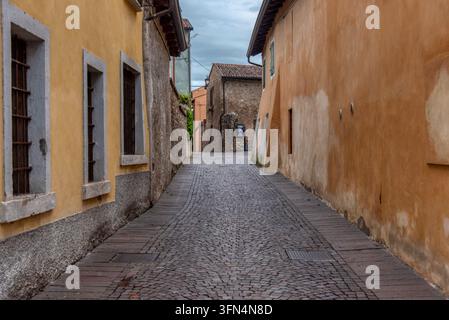 Rue pavée tranquille bordée de bâtiments rustiques en plâtre jaune et terre cuite menant au centre historique du village médiéval de Borghetto sul Banque D'Images