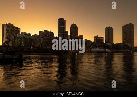 Coucher de soleil sur le centre-ville de Boston, États-Unis, vu à travers le port depuis le Seaport District, avec des yachts amarrés et des bâtiments riverains. Banque D'Images