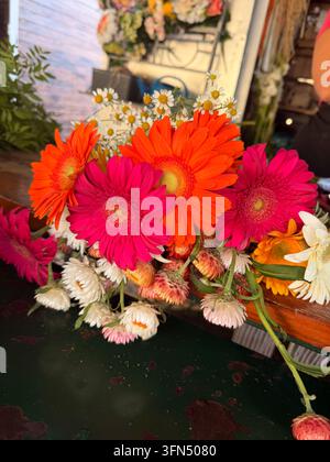 Close-up d'un bouquet coloré avec des fleurs semblables à des gerberas roses et orange et de petites fleurs blanches sur une surface sombre. Banque D'Images
