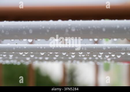 Une vue macro rapprochée de gouttes de pluie claires suspendues sous les barres blanches d'un séchoir extérieur après une averse fraîche Banque D'Images