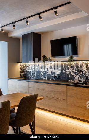 Vue intérieure d'une cuisine moderne comportant des placards inférieurs en bois, un plan de travail noir et un dosseret en marbre sombre frappant. L'espace contemporain i Banque D'Images