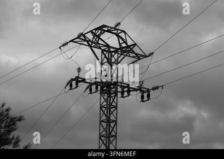 Photographie en noir et blanc d'un grand pylône électrique en métal et des lignes de transmission sous un ciel nuageux Banque D'Images