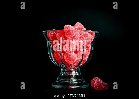 Bonbons en gelée en forme de cœur rouges enrobés de sucre dans un bol en verre sur un fond sombre avec espace de copie. Banque D'Images