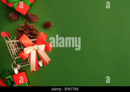 Concept de shopping de Noël avec un mini chariot de courses et des cadeaux sur fond vert Banque D'Images