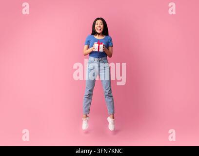 Concept de célébration. Photo pleine longueur de sauter haute excitée jeune femme asiatique tenant une boîte-cadeau enveloppée avec cadeau, regardant surpris dans le poêle isolé Banque D'Images