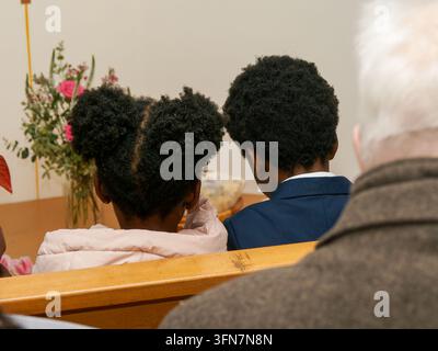 Deux enfants assis sur un banc en bois vus de dos lors d'un événement. Banque D'Images