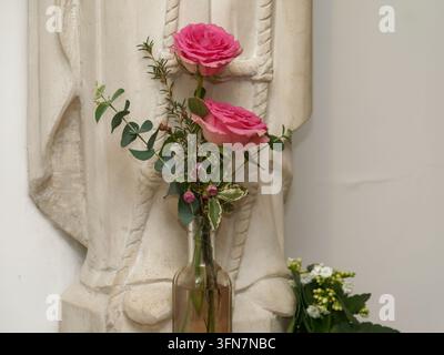 Roses roses dans un vase en verre placé devant une statue en pierre à l'intérieur. Banque D'Images