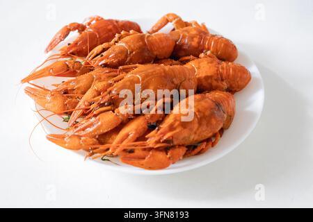 tas de crevettes cuites appétissantes sur une assiette blanche, vue de dessus. Écrevisses rouges fraîchement bouillies ou homards d'eau douce, assaisonnés d'aneth, prêts à être mangés comme s Banque D'Images
