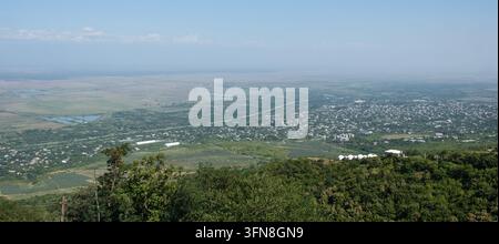 Panorama élevé montrant des sighnaghi répandus dans la vallée, avec des collines boisées au premier plan, des champs cultivés, des bâtiments dispersés et des montagnes brumeuses b Banque D'Images