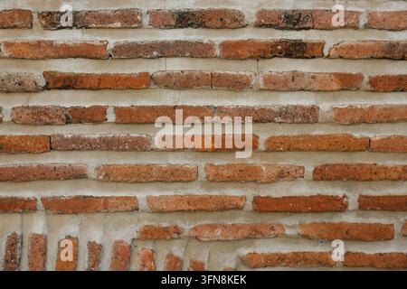 Vue rapprochée de briques rouges vieillies disposées en rangées horizontales inégales avec un mortier pâle, des surfaces patinées et une texture de maçonnerie rustique sur le mur Banque D'Images