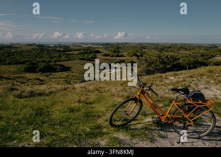 Vélo orange garé sur l'herbe surplombant des collines vertes, eau an Banque D'Images