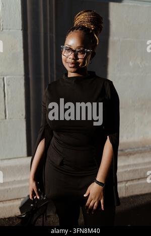 Femme noire élégante avec des tresses souriant au soleil Banque D'Images