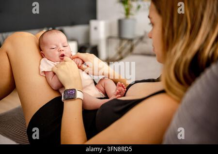 Une mère aimante touche le visage du nourrisson tout en se reposant sur le canapé lors d'une séance de lien tranquille en journée Banque D'Images