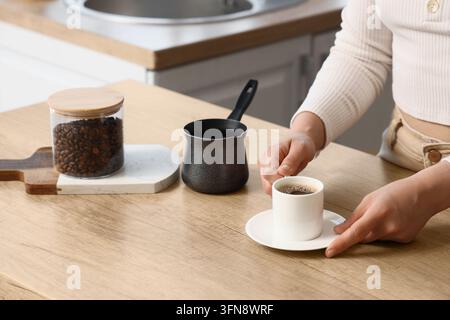 Routine du café du matin et style de vie, femme tenant une tasse d'espresso frais dans une cuisine moderne avec des grains de café et une pot turque traditionnelle Banque D'Images