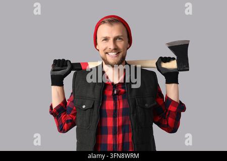 Travail acharné et travail manuel, bûcheron souriant tenant une hache sur ses épaules, portant un bonnet rouge et une chemise à carreaux pour la construction ou la foresterie Banque D'Images